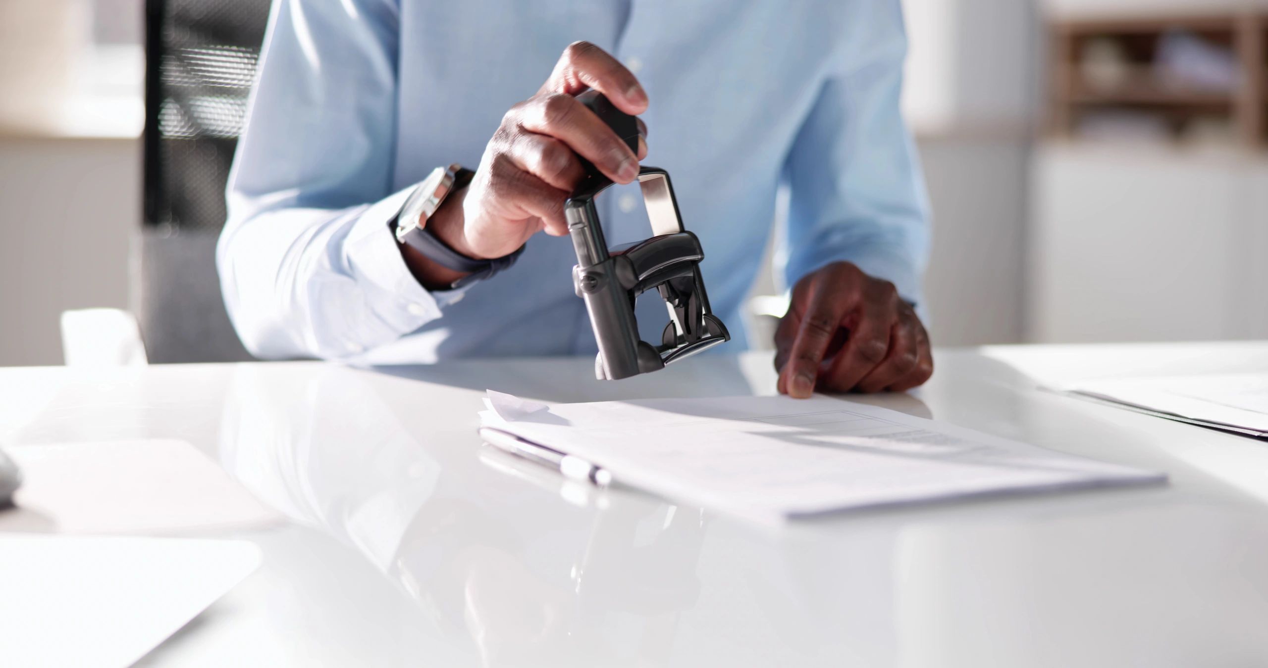Person stamping documents at a desk with a pen nearby.