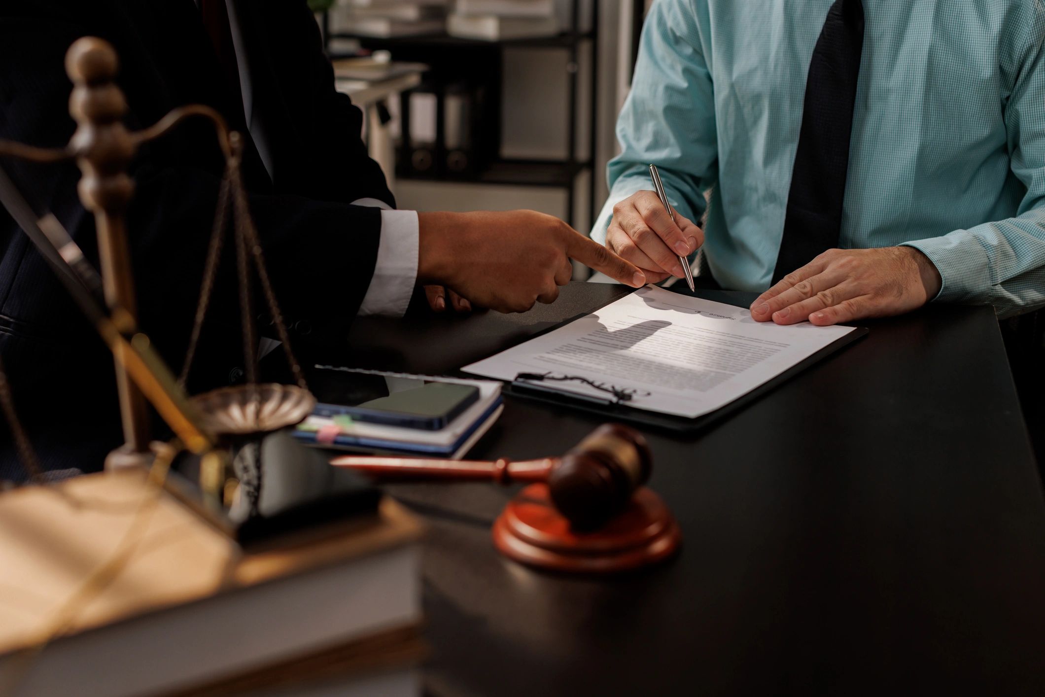 Two professionals shaking hands over a signed contract at a desk.