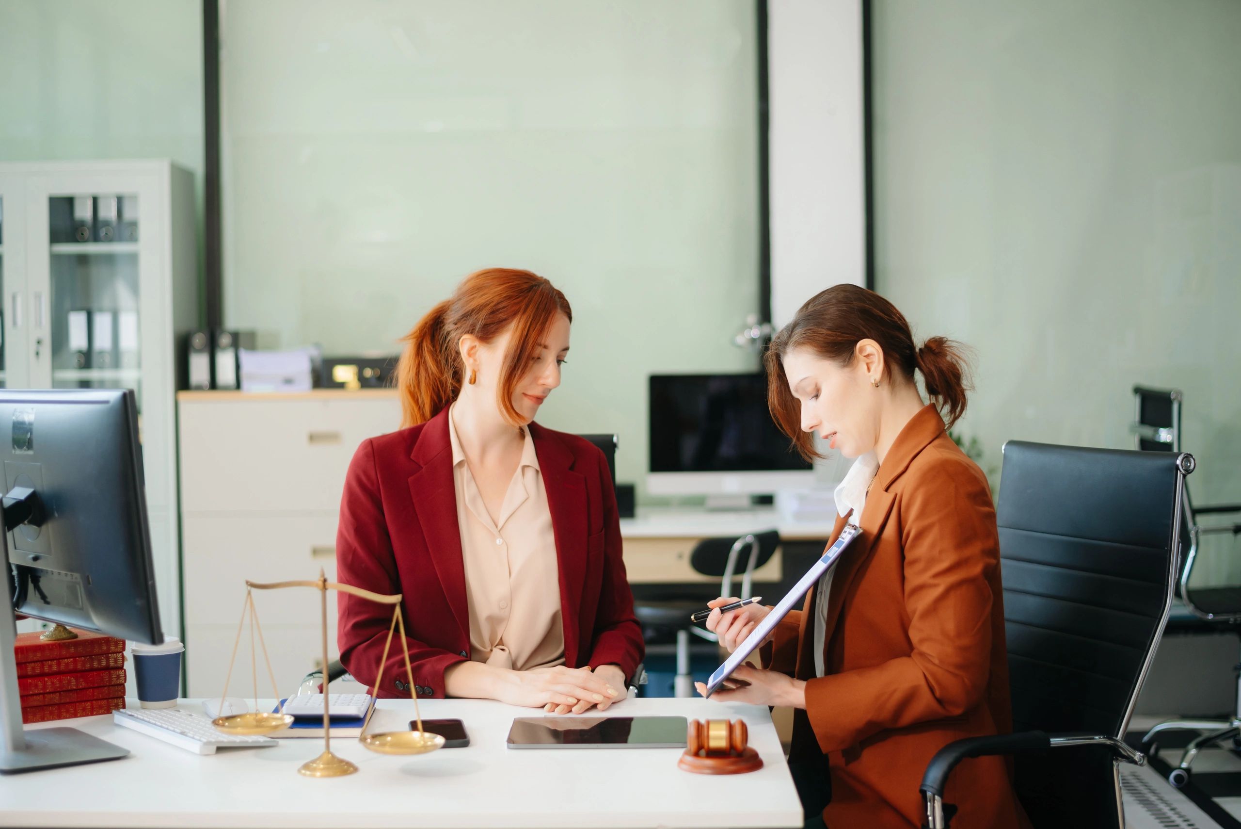 Two women engaged in a focused discussion at a desk with notebooks and coffee.
