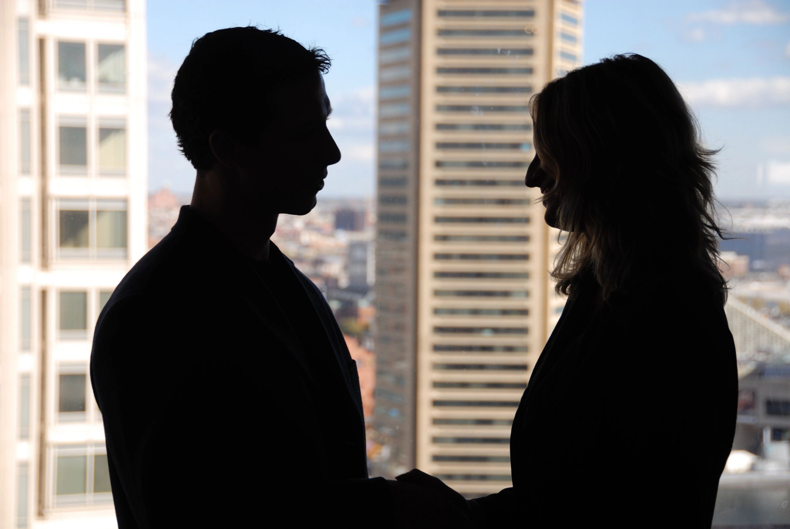 Silhouettes of two people facing each other against a cityscape background.