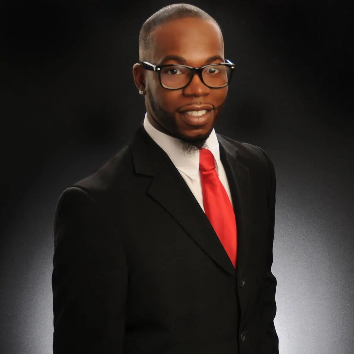 Professional man in a black suit with a red tie against a dark background.